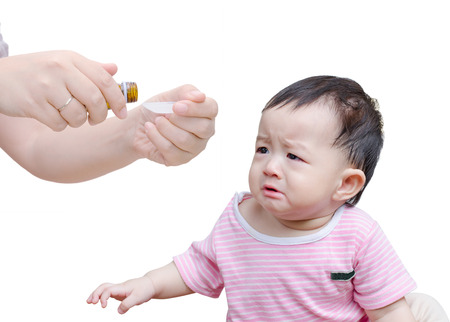 43163449 - woman's hands pouring medicine in a spoon foreground and crying baby over white background