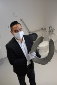 Dr. Wong (then with VCH) in November 2021, with one of the copper toilet seats installed in Lions Gate Hospital as part of the hospital's disinfection program (North Shore News).